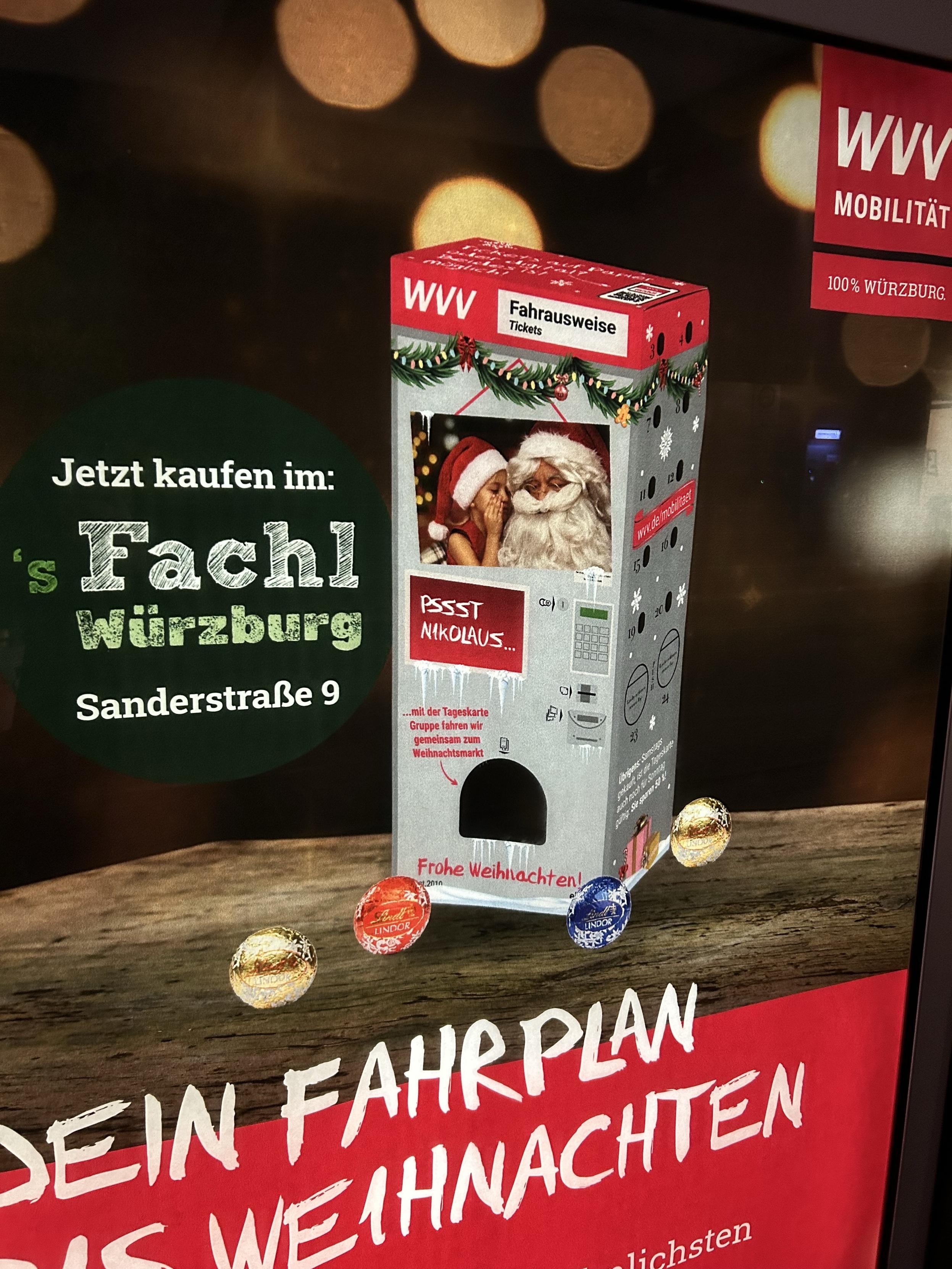 The image features an advertisement promoting tickets for public transport in Würzburg. It shows a ticket dispenser decorated for Christmas, with a photo of a child whispering to Santa Claus. The background has festive lights, and there are also three decorative chocolates in front